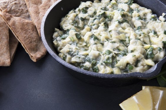 Cast iron pan of spinach artichoke dip surrounded by pita chips