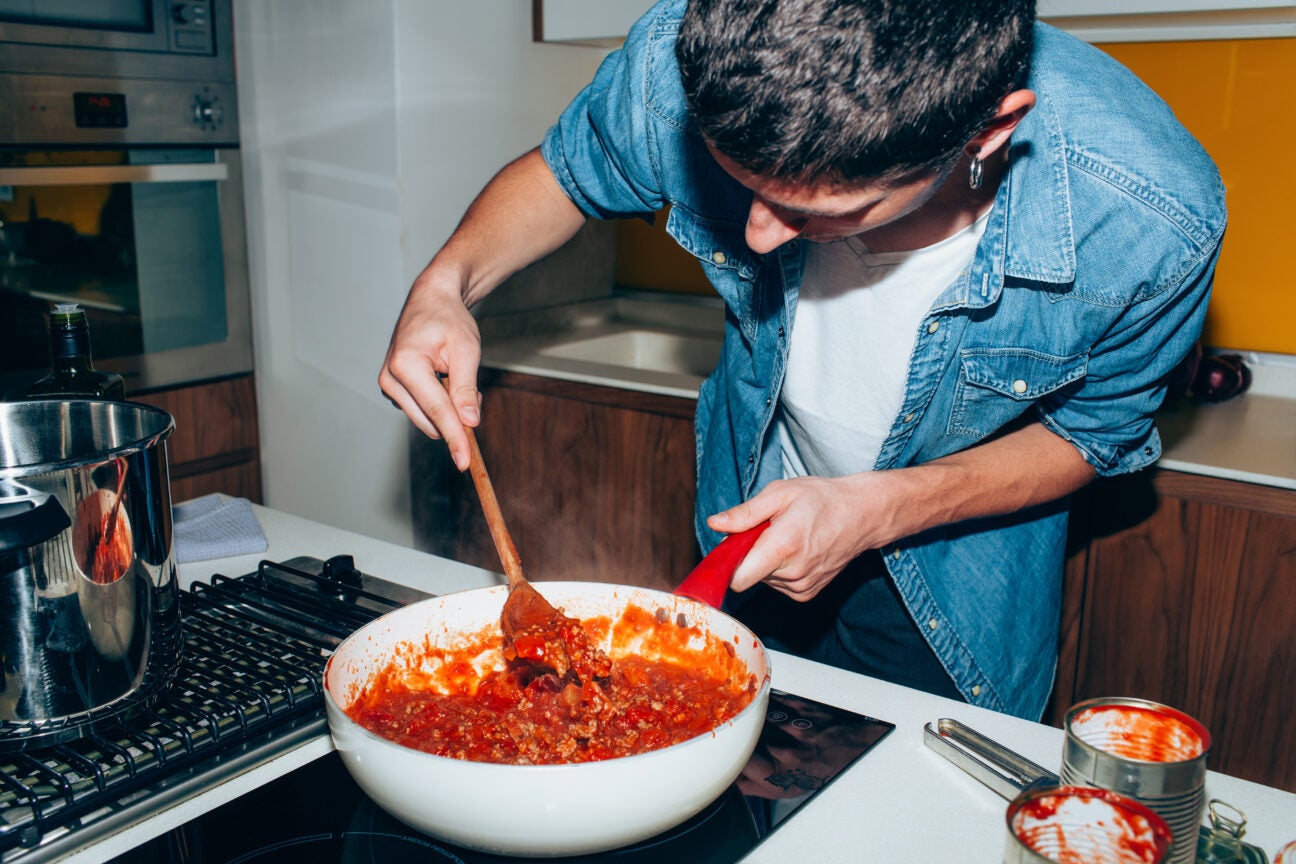 man stirring tomato sauce with veggies