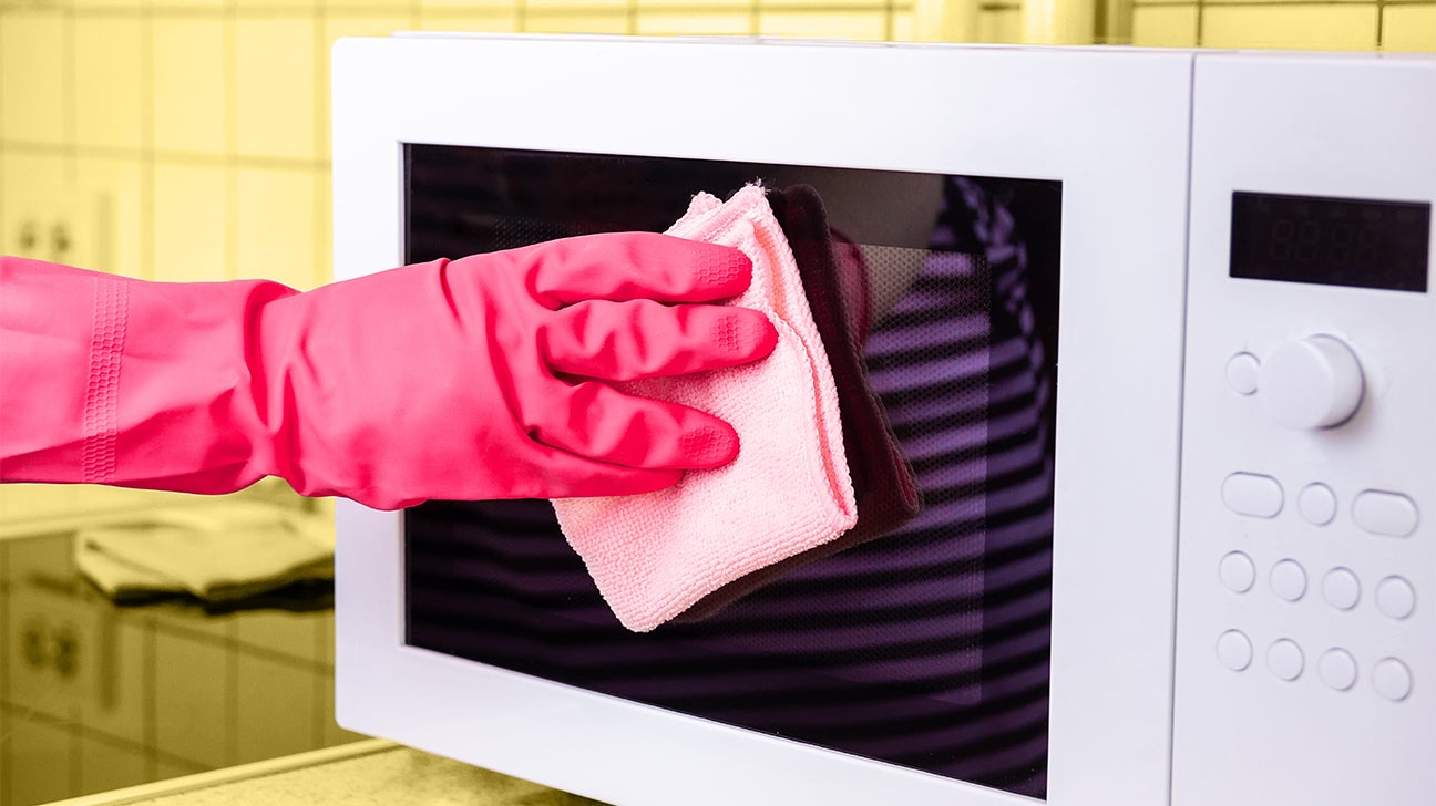 a hand wiping off the front of a microwave