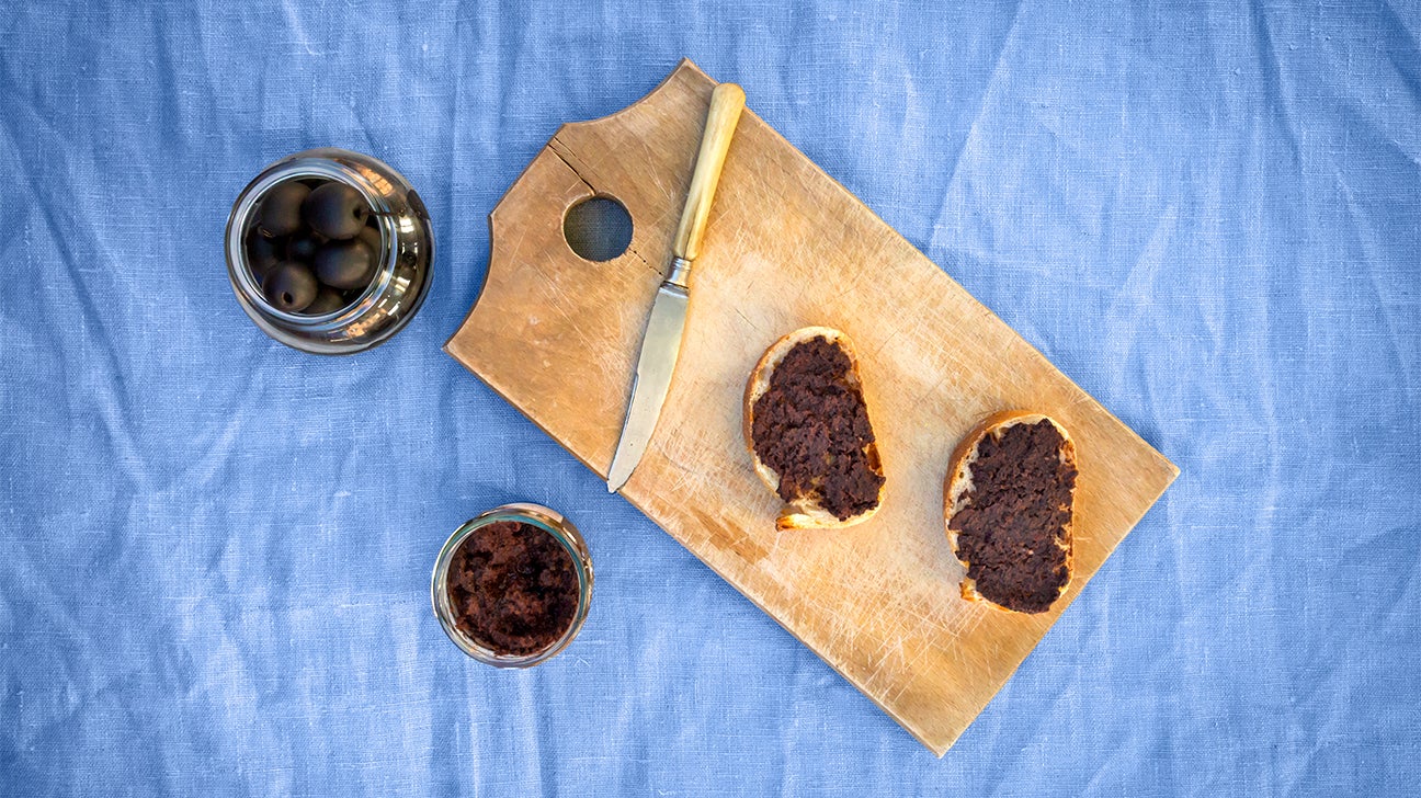 an overhead shot of olive tapenade on crusty bread on a wooden serving board