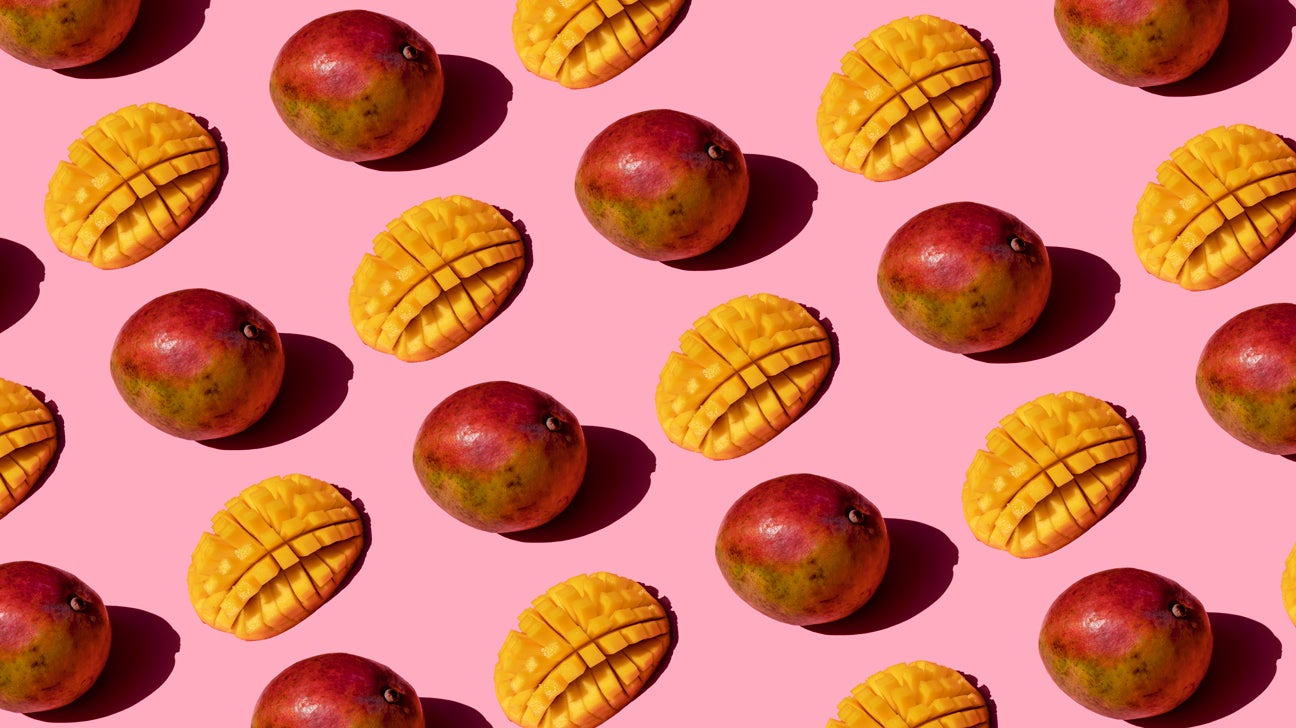 Whole and cut mangoes on a pink background