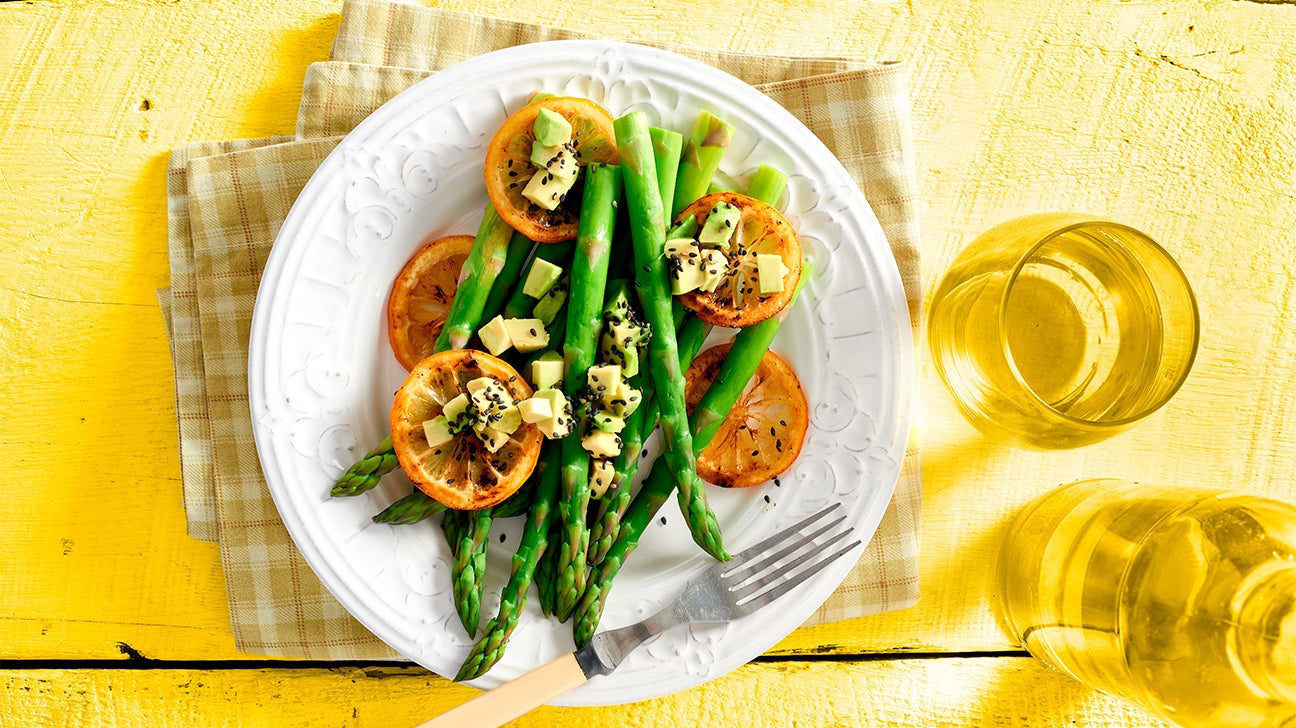 plate of asparagus, lemons, and avocado on yellow background