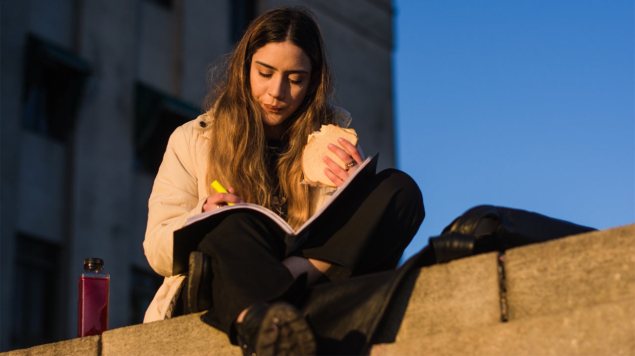 young woman eating a sandwich and studying