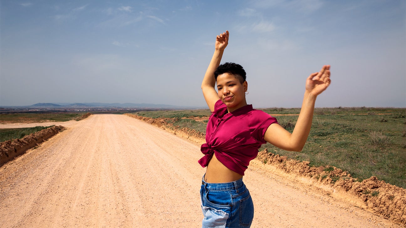 Woman with hands up, blue sky and open road in background